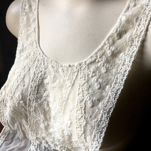 May include: White lace tank top with a delicate floral pattern. The tank top is sheer and has a scoop neck.