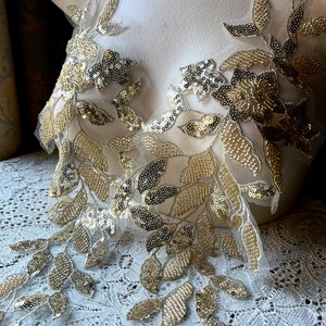 Könnte beinhalten: Goldene und silberne florale Spitzenborte mit Pailletten und Perlen. Die Borte ist auf weißem Hintergrund.
