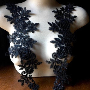 Könnte beinhalten: Zwei schwarze Spitzenapplikationen mit floralen Designs, mit zarten Blättern und Rosen. Die Applikationen sind perfekt, um Kleidung oder Bastelarbeiten einen Hauch von Eleganz zu verleihen.