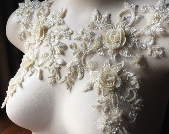 May include: A delicate ivory lace applique with floral designs and pearl-like embellishments. The applique features intricate floral patterns and delicate beading, perfect for adding a touch of elegance to a garment.