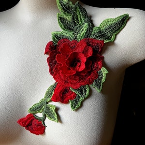 May include: Red embroidered flower applique with green leaves. The flower has a layered, 3D effect and is perfect for adding a touch of elegance to clothing or crafts.