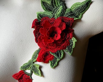 May include: Red embroidered flower applique with green leaves. The flower has a layered, 3D effect and is perfect for adding a touch of elegance to clothing or crafts.