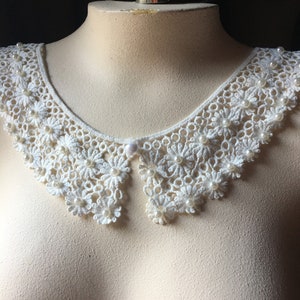 Puede incluir: Collar de encaje blanco con adornos de perlas. El collar est&aacute; en un busto de maniqu&iacute; blanco.