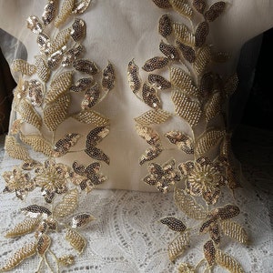May include: Gold sequined floral and leaf appliques. The appliques feature intricate detailing with gold sequins and beads, creating a shimmering effect. The design includes floral and leaf patterns, suitable for embellishing garments or crafts.