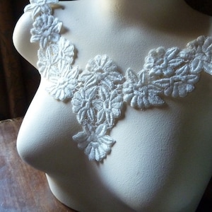 May include: White lace trim with a floral design. The lace is delicate and intricate, with a scalloped edge.