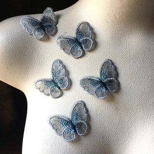 May include: Five silver and blue butterfly appliques with a glittery finish. The appliques are on a white surface.