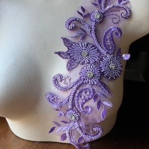 May include: Purple beaded floral applique with rhinestones. This delicate embellishment features a floral design with intricate details and sparkling accents.
