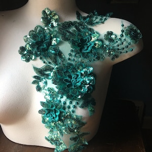 May include: Teal green floral applique with sequins and beads. The applique is on a white mannequin form.