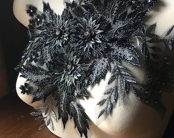 Puede incluir: Aplique de encaje negro con diseño floral. El aplique presenta detalles intrincados y una textura delicada.
