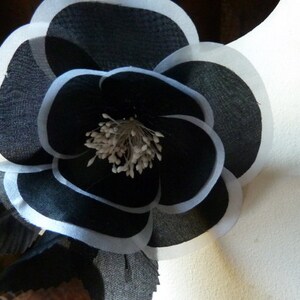 May include: A black and white fabric flower with a white center. The flower is layered and has a ruffled edge.