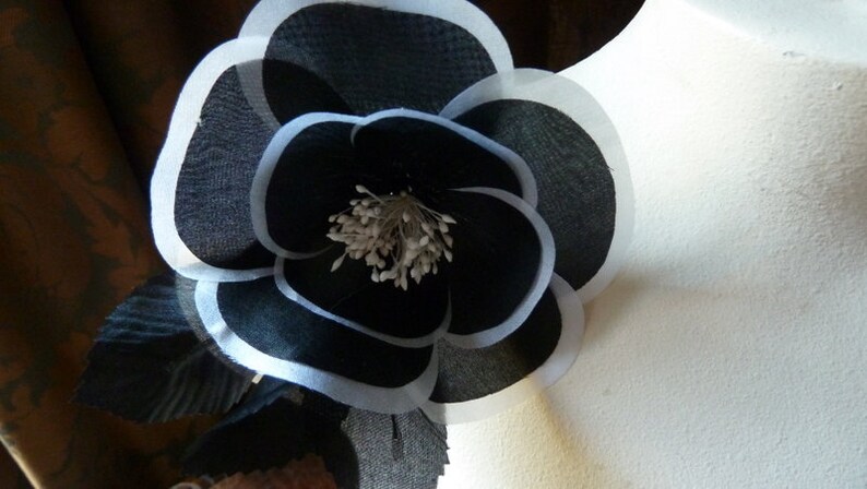 May include: A black and white fabric flower with a white center. The flower is layered and has a ruffled edge.