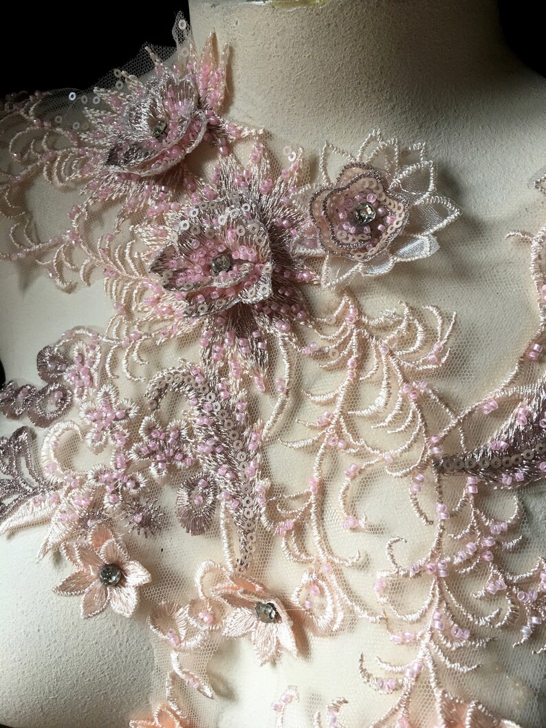 May include: Pink and beige floral lace applique with beaded details. The lace features delicate floral designs and intricate beading.