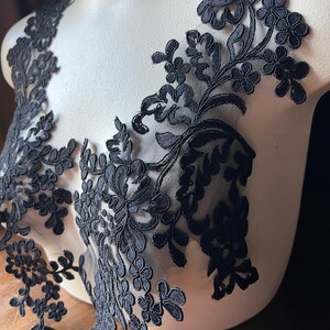 Puede incluir: Borde de encaje floral negro con un dise&ntilde;o delicado. El encaje est&aacute; en un maniqu&iacute; blanco.