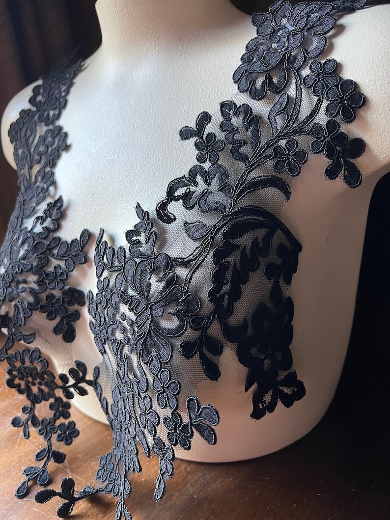 Puede incluir: Borde de encaje floral negro con un dise&ntilde;o delicado. El encaje est&aacute; en un maniqu&iacute; blanco.
