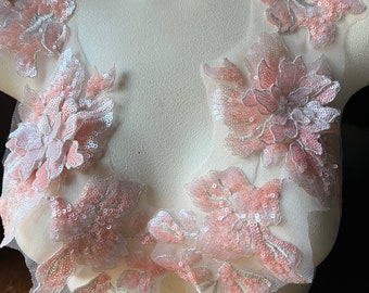 May include: Pink floral lace applique with sequins. The applique is made of delicate tulle and features a variety of flower shapes. The sequins are scattered throughout the applique, adding a touch of sparkle.