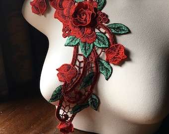 Op de afbeelding: Rode en groene geborduurde bloemenapplicatie met een paisley-ontwerp. De applicatie heeft een grote roos met kleinere rozen en bladeren.