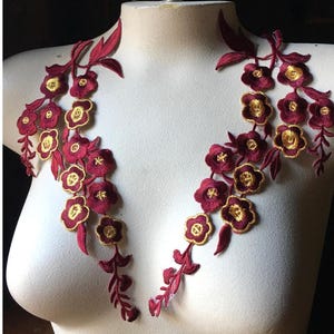 Peut inclure: Deux appliques florales bordeaux avec des accents dorés. Les appliques sont en tissu et ont un design délicat et féminin.