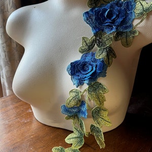 May include: A blue and green floral applique with three blue roses and green leaves. The applique is on a white mannequin.