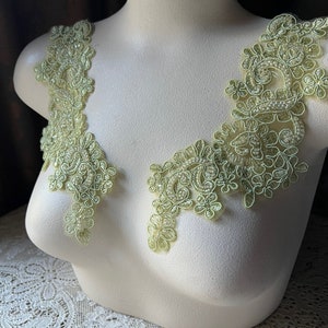 May include: Two pieces of green beaded lace trim with floral designs. The lace is on a white dress form.