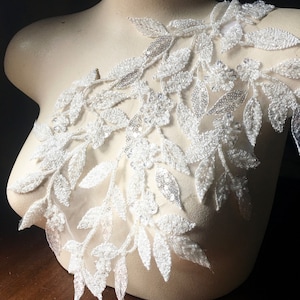 May include: White beaded lace trim with a floral design. The trim features delicate leaves and small flowers with sequins. This trim is perfect for adding a touch of elegance to any project.