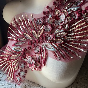 May include: Red and gold floral applique with sequins and beads on a sheer mesh fabric. This embellishment is perfect for adding a touch of sparkle and elegance to any garment.