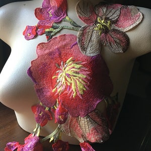Pode incluir: Um conjunto de apliques florais bordados em tons de rosa, vermelho, amarelo e castanho. Os apliques apresentam uma flor grande com um centro amarelo e flores menores com pétalas cor-de-rosa.