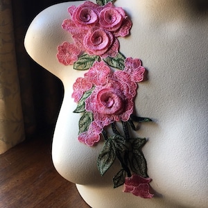 Puede incluir: Aplique floral rosa y verde con un grupo de tres rosas grandes y flores más pequeñas. El aplique está hecho de tela y es adecuado para coser o manualidades.