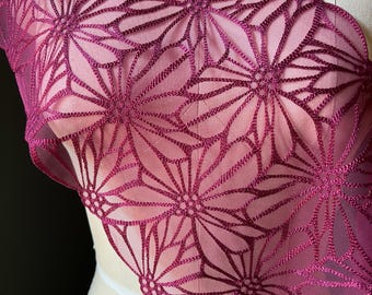 May include: Close-up of a sheer, magenta-colored fabric with a floral pattern. The design features large, stylized flowers with intricate stitching. The fabric has a scalloped edge and is draped over a mannequin.