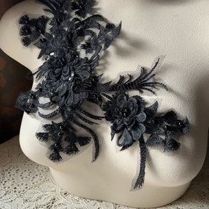 May include: Black lace applique with beaded embellishments. The applique features a floral design with delicate leaves and intricate details.