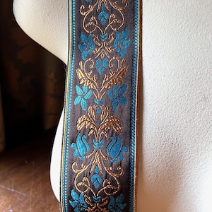 May include: A decorative ribbon with a dark brown background and a repeating floral pattern in teal and gold. The ribbon has a teal border and is displayed against a neutral background.