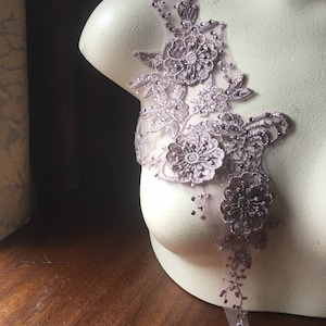 Op de afbeelding: Een delicate bloemvormige kantenapplicatie in een roze blush-kleur met glinsterende versieringen. De applicatie heeft een cluster van bloemen en bladeren, perfect om een ​​tikje elegantie toe te voegen aan een kledingstuk of handwerkproject.