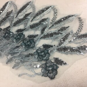 May include: Silver and black floral embroidery with sequins on a sheer fabric. The embroidery features leaves and flowers.