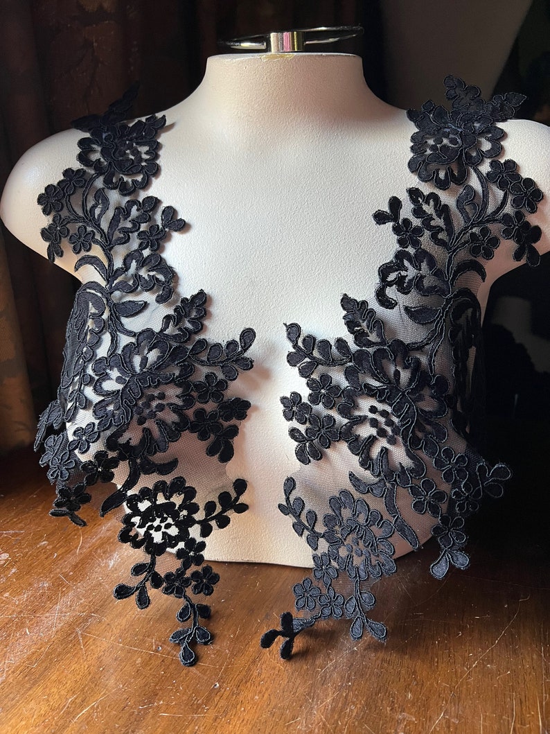Puede incluir: Dos aplicaciones de encaje negro con dise&ntilde;os florales. Las aplicaciones est&aacute;n en una forma de maniqu&iacute; blanca.