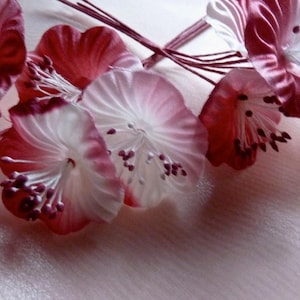 May include: Close-up of a cluster of artificial flowers. The petals are a gradient of white to deep red, with delicate stamens. The flowers are arranged on a soft, light pink surface, creating a romantic and delicate aesthetic.