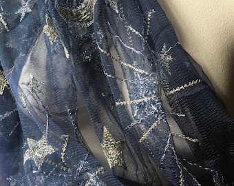 May include: A sheer navy blue fabric featuring intricate embroidery of crescent moons and stars in metallic gold and silver thread. The lightweight material has a fine mesh texture with visible stitching patterns that create a celestial design.