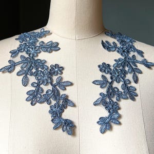 May include: Two blue floral lace appliques. Each applique features a delicate design of flowers and leaves. The appliques are displayed on a mannequin, showcasing their potential use in garment decoration or craft projects.