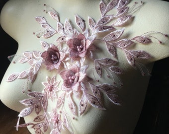 Puede incluir: Una delicada aplicación floral con flores y hojas rosas, acentuada con pequeñas cuentas de perlas. Esta decoración de encaje es perfecta para agregar un toque de elegancia a la ropa o las manualidades.