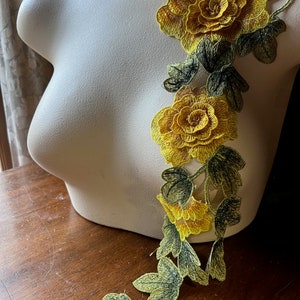 May include: Yellow floral embroidery with green leaves. The embroidery is on a white background.