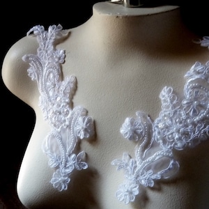 May include: White lace appliques with floral and scroll designs are displayed on a mannequin. The delicate lace features small, round embellishments and intricate patterns, perfect for bridal or craft projects.