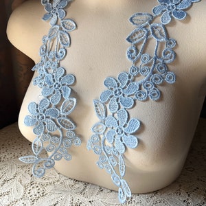 May include: Two pieces of light blue floral lace trim. The lace is delicate and features a floral design with leaves and small circles.