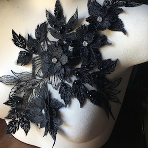 May include: Black lace applique with floral designs and rhinestones. The applique is on a white mannequin bust.