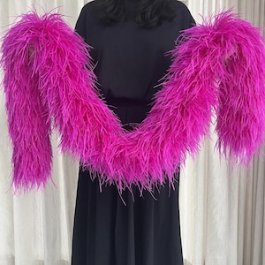 May include: A long, vibrant hot pink feather boa made of soft, wispy plumes. The accessory features a dense, voluminous texture with a consistent bright magenta color throughout, creating a full and fluffy appearance across its entire length.