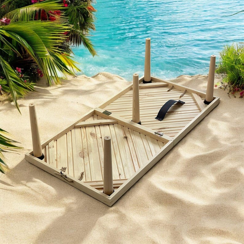 May include: A wooden folding table with a chevron pattern on the top. The table has six legs and a black handle. The table is folded up and lying on a sandy beach.