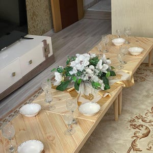 May include: A wooden table with a chevron pattern top, set for a meal with white bowls, clear glasses, and a white floral centerpiece.