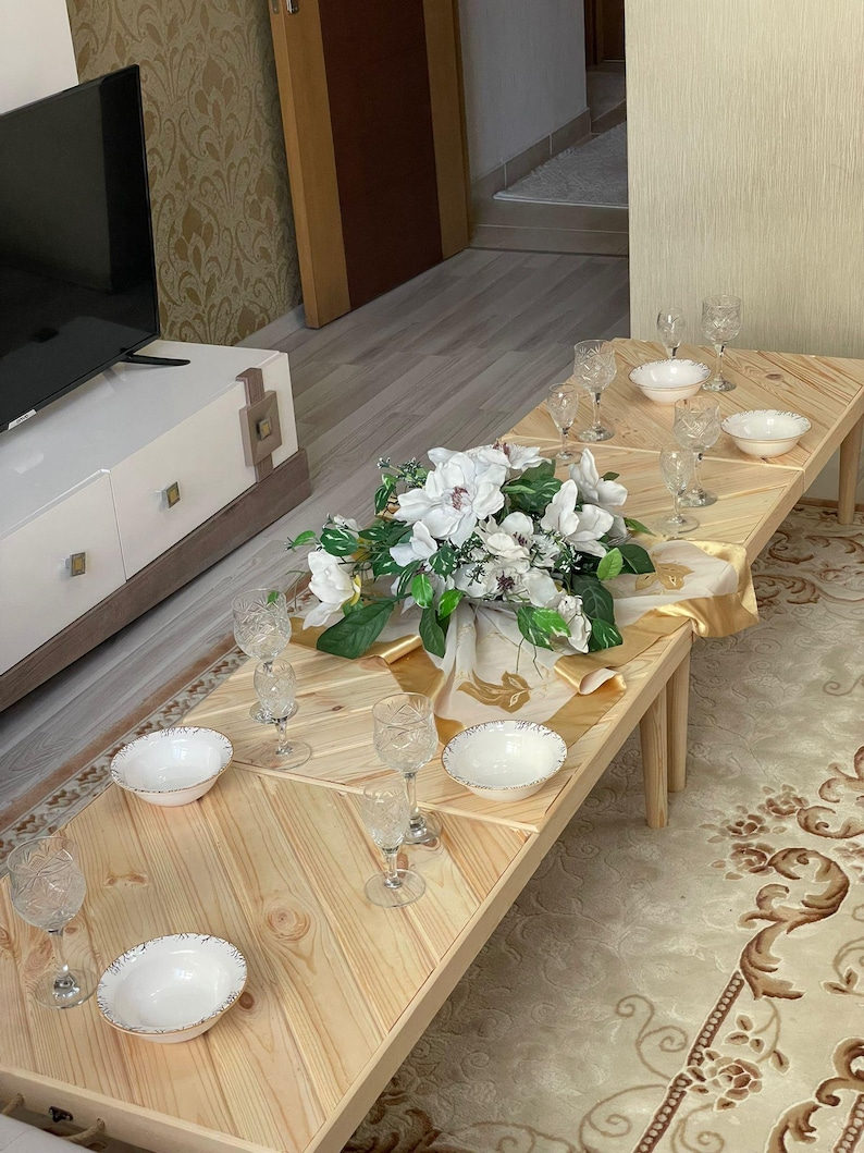 May include: A wooden table with a chevron pattern top, set for a meal with white bowls, clear glasses, and a white floral centerpiece.