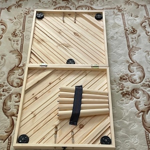 May include: A wooden game board with a rope handle and black rubber feet. The board is open and shows a set of wooden dowels with a black strap.