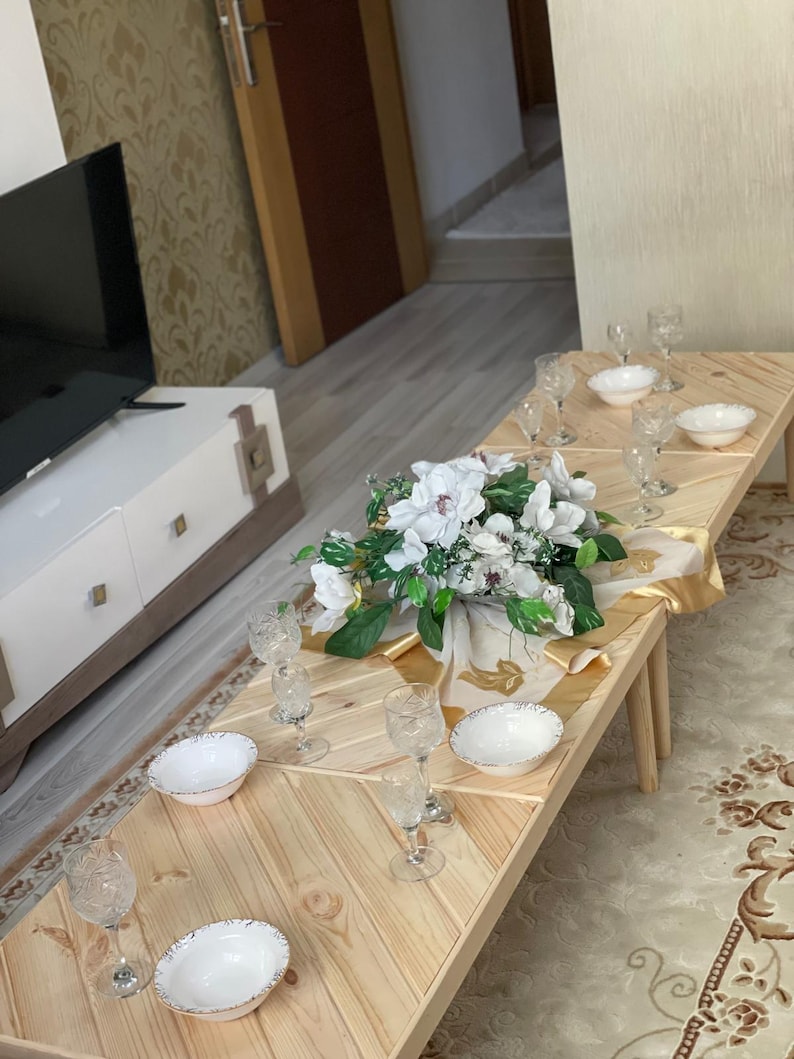 May include: A wooden table set with white bowls and clear glass cups. The table is made of light wood planks and has a chevron pattern. A bouquet of white flowers is in the center of the table.