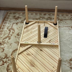 May include: A wooden table with a striped top and six legs. The table is folded in half and the legs are folded up.