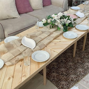 May include: A rustic wooden table set with white plates and a beige tablecloth. The table is decorated with a bouquet of white flowers and has a chevron pattern.