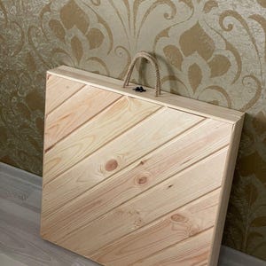 May include: A wooden box with a diagonal wood grain pattern and a rope handle. The box is closed and has a metal latch.